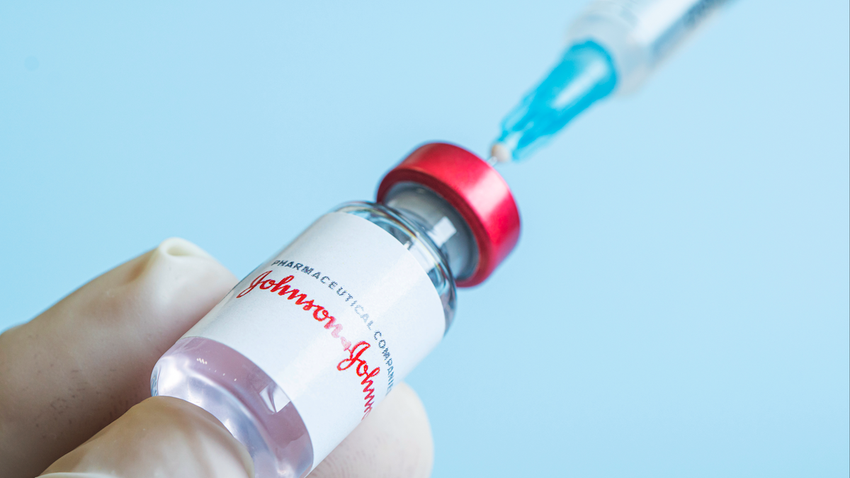 Gloved hand holds Johnson & Johnson vaccine vial with syringe, representing pharmaceutical and vaccination concepts.