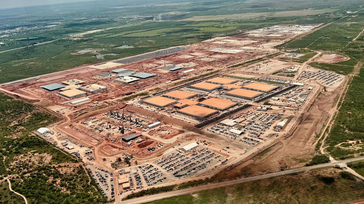Aerial view of a large, partially constructed data center surrounded by parked vehicles and red soil in Abilene, Texas